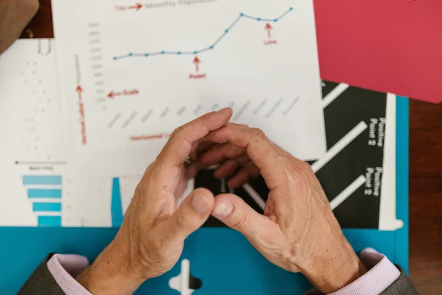 Hands examining financial graphs and charts on a wooden desk, indicative of business planning. Prognozy zatrudnienia: jak czytać dane o popycie na zawody